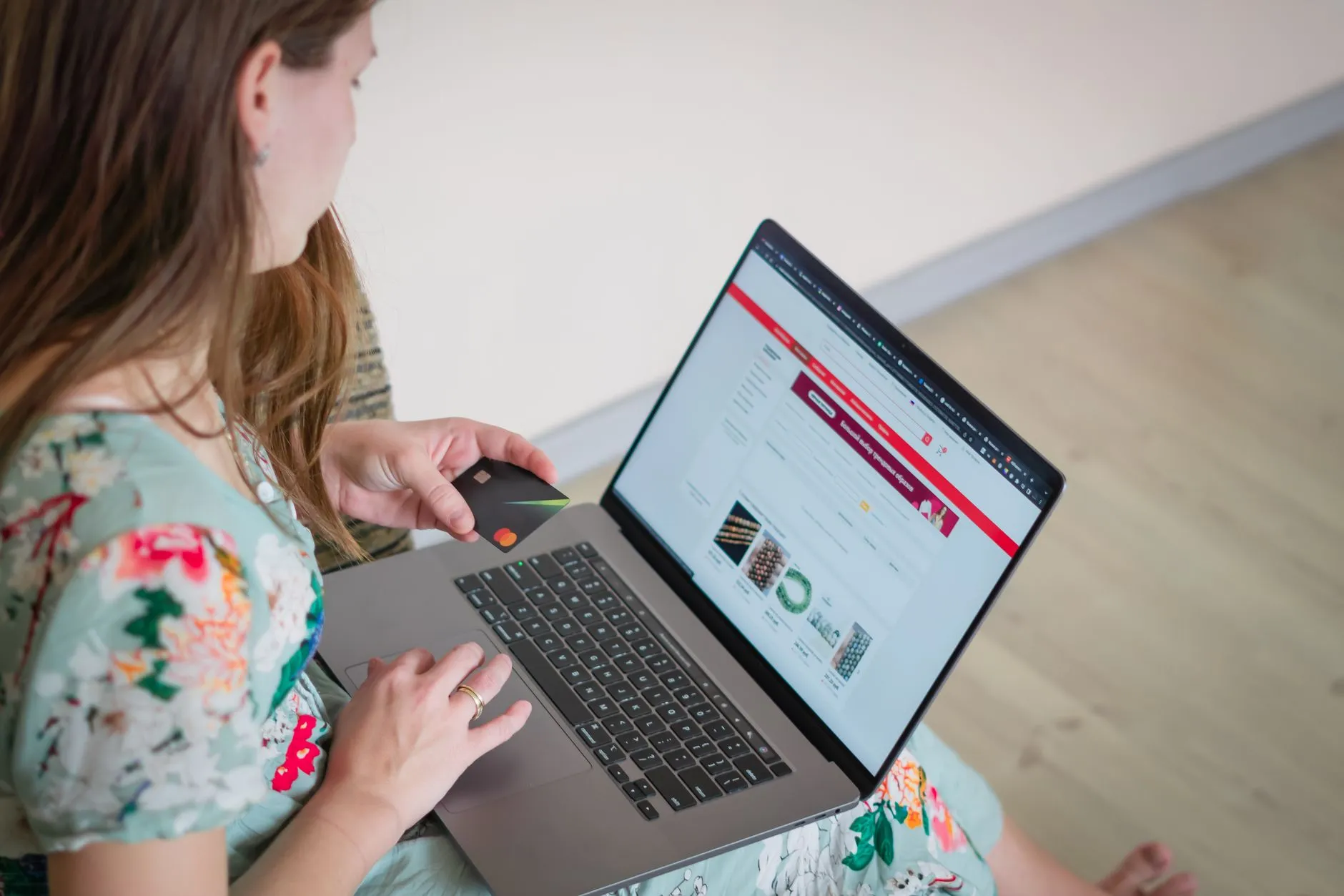 Mulher segurando um cartão de débito enquanto usa o notebook