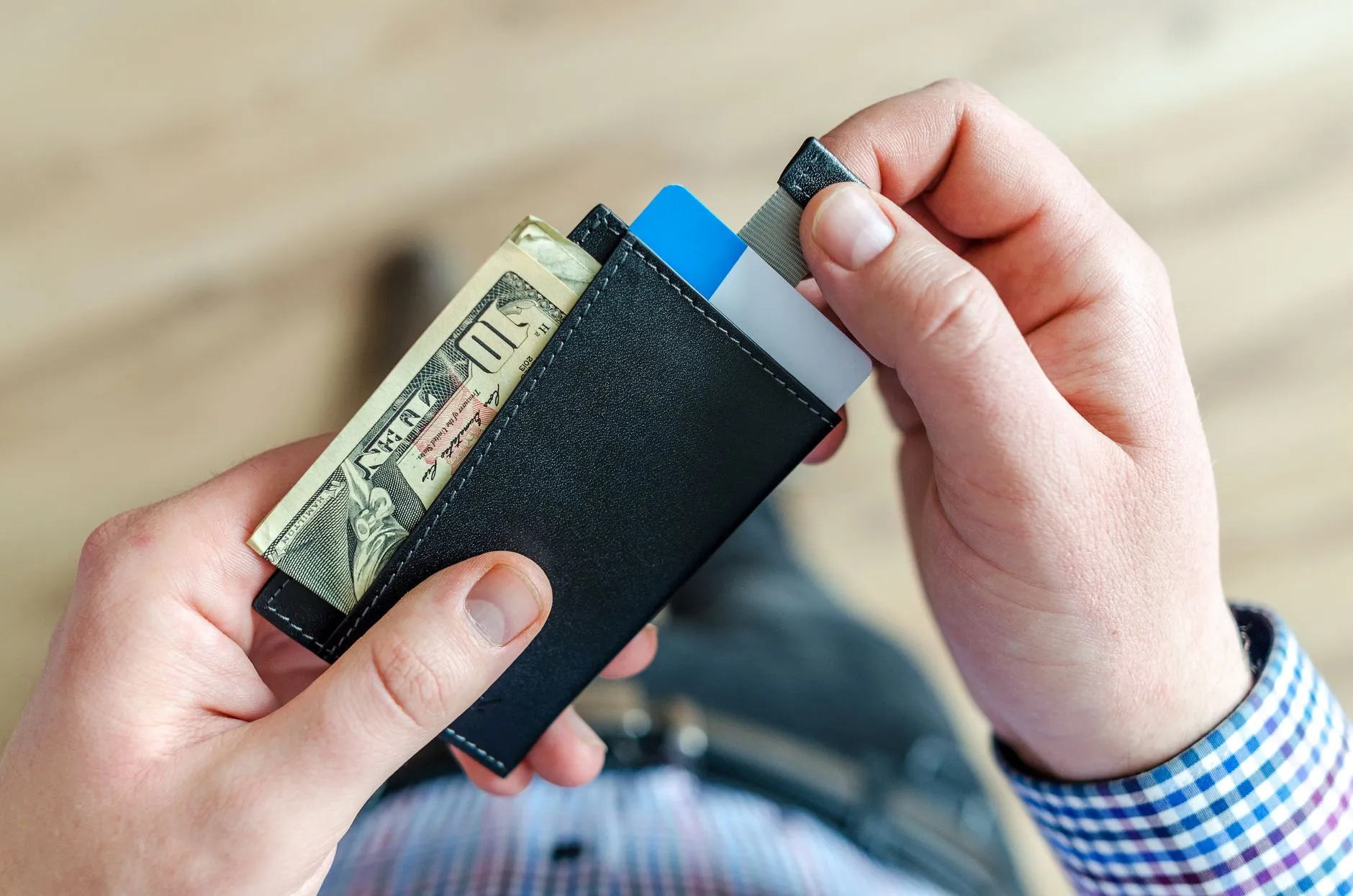 Mãos segurando uma carteira com notas de dólar e cartões