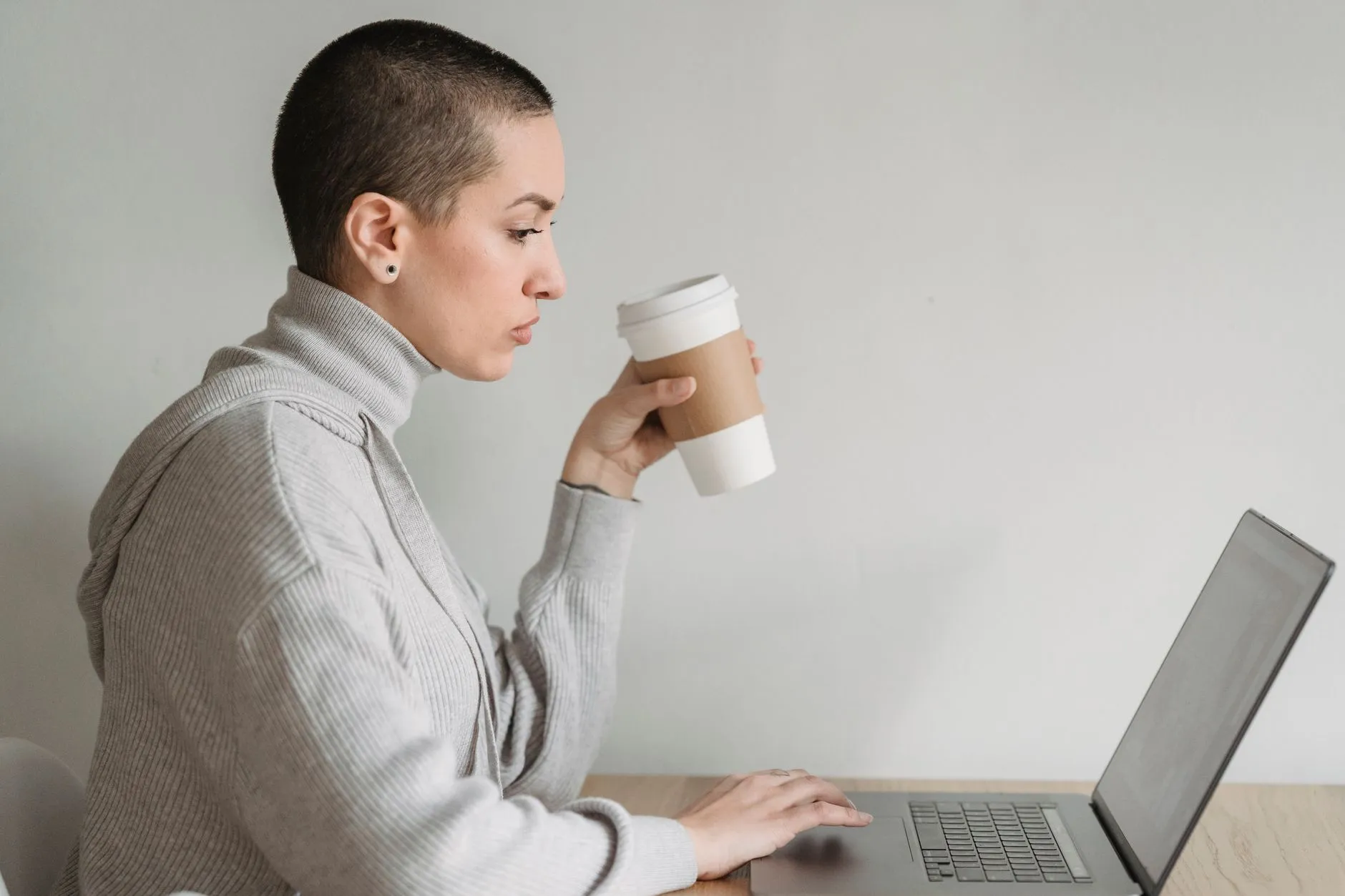 Mulher tomando café enquanto trabalha no notebook