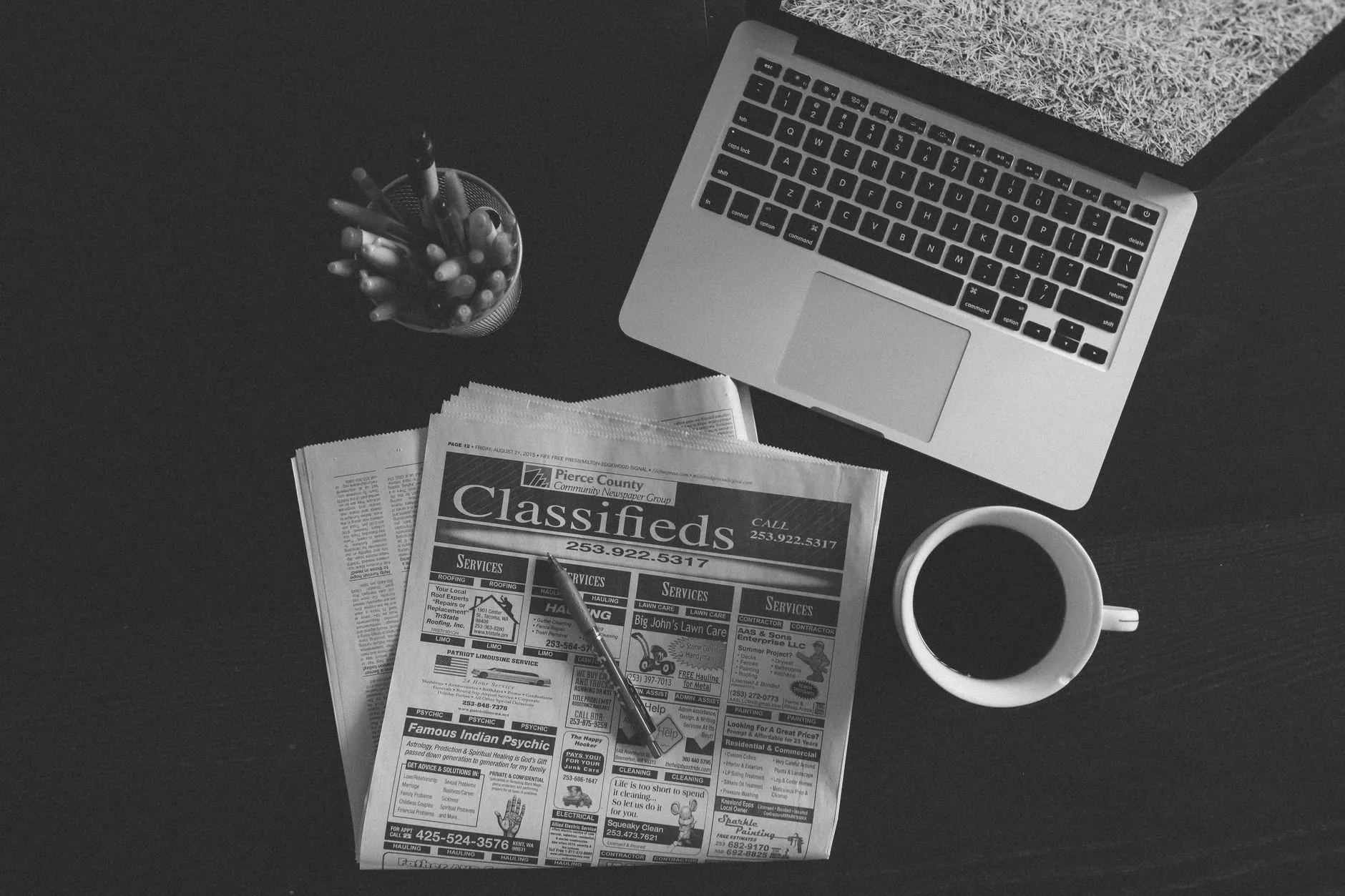 Notebook, café e jornal aberto na seção de classificados
